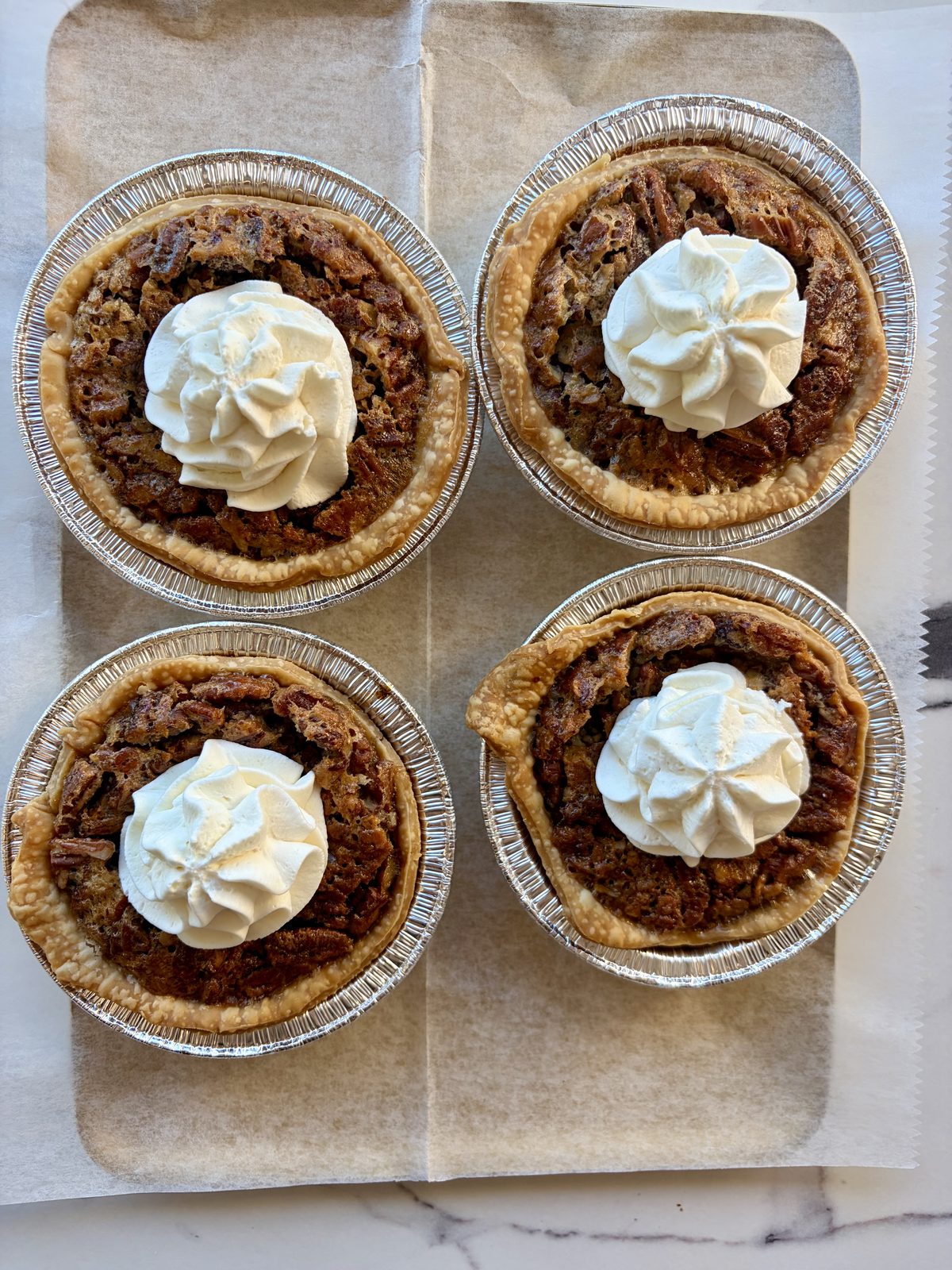 Four pecan pies topped with whipped cream